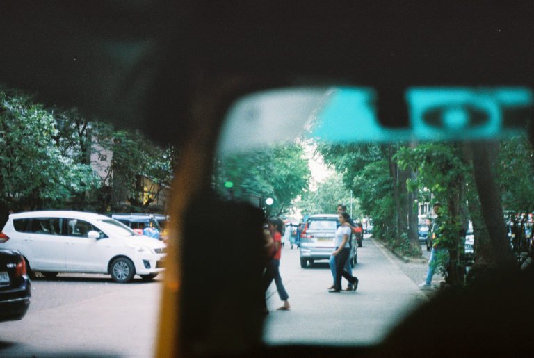 A street seen through a car's wing mirror, traffic and pedestrians beyond the frame