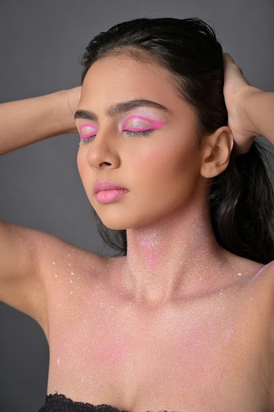 Graphic pink eye makeup, glitter across the shoulders, eyes closed with hands in the hair