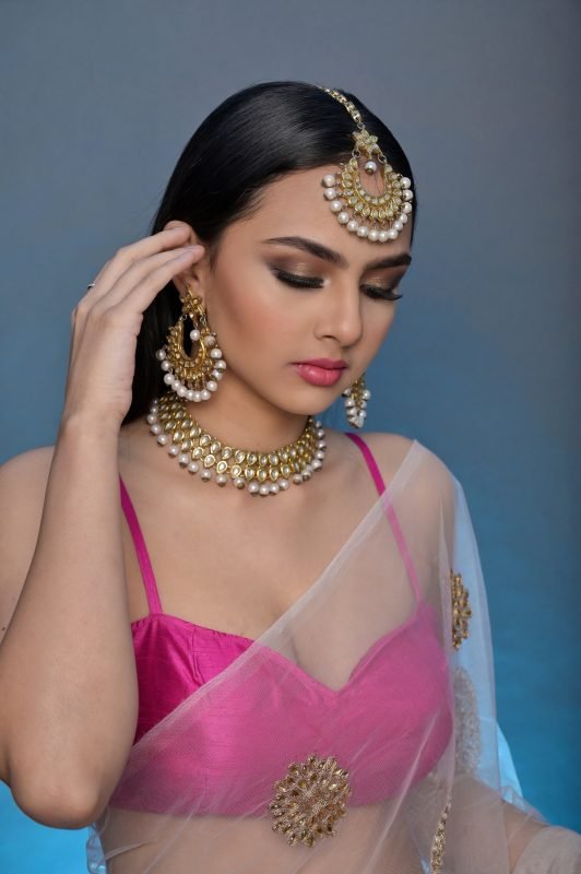 Bridal makeup: a model with eyes lowered, gold kundan jewellery and a maang tikka, hand raised to her earring