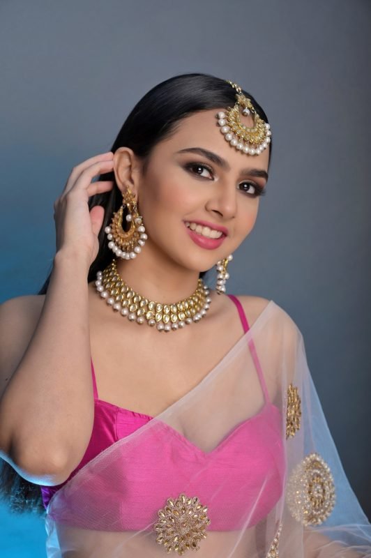 Bridal makeup: a model smiling, adjusting a gold jhumka earring, pink lehenga and sheer dupatta