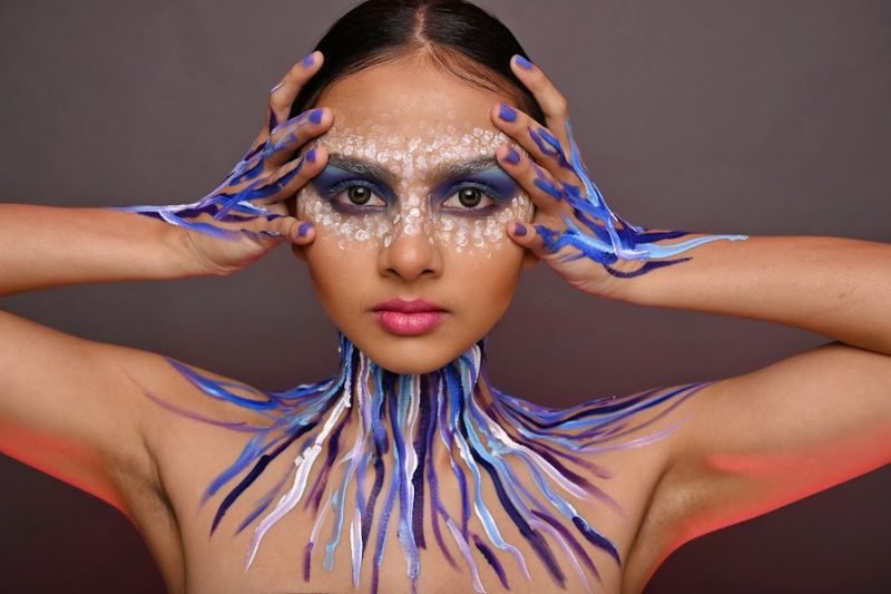 Editorial makeup: hands framing the face, blue and purple paint running down the neck