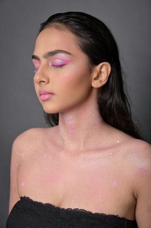 Pink blush and glitter makeup on bare shoulders, black strapless top, grey backdrop