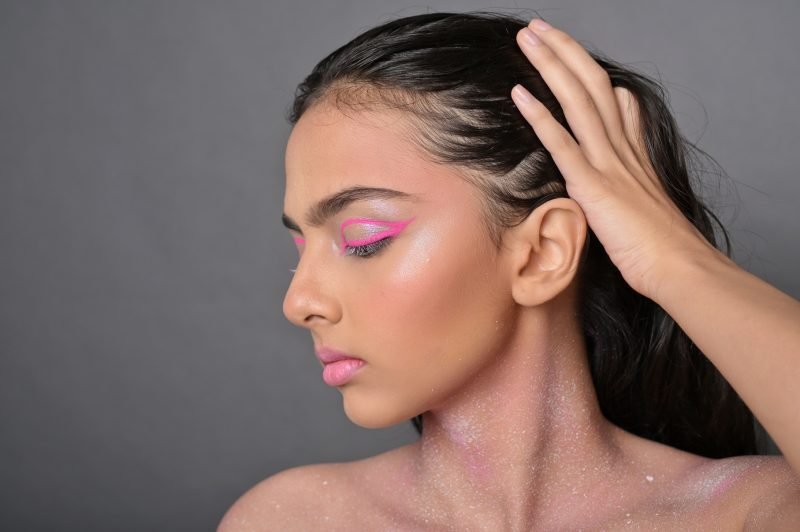Profile portrait: graphic pink eye makeup and glitter, hand sweeping back the hair