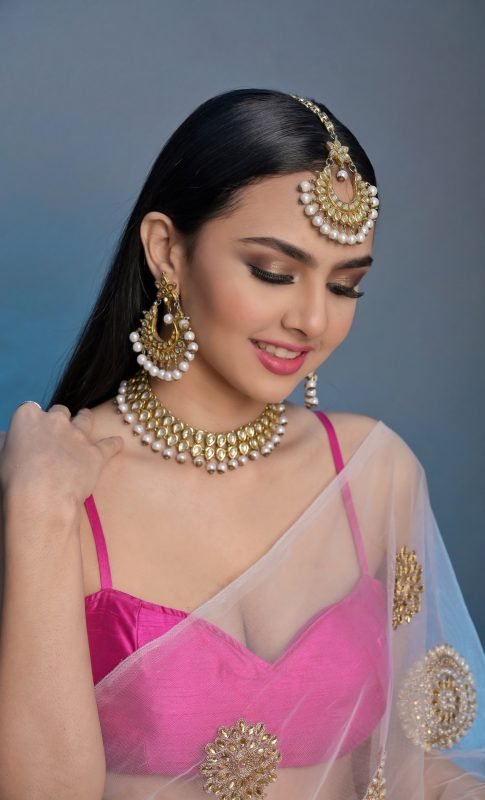 Bridal makeup: a model smiling in a pink lehenga and gold kundan jewellery, blue backdrop