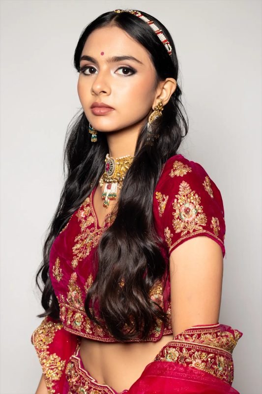 Bridal makeup: a model in a red and gold lehenga against a pale backdrop