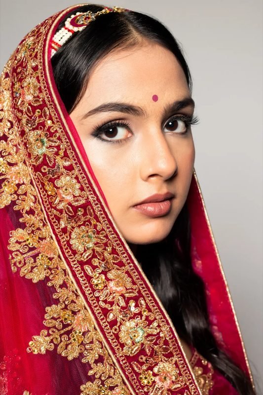 Close bridal portrait: a red dupatta with a gold border framing the face