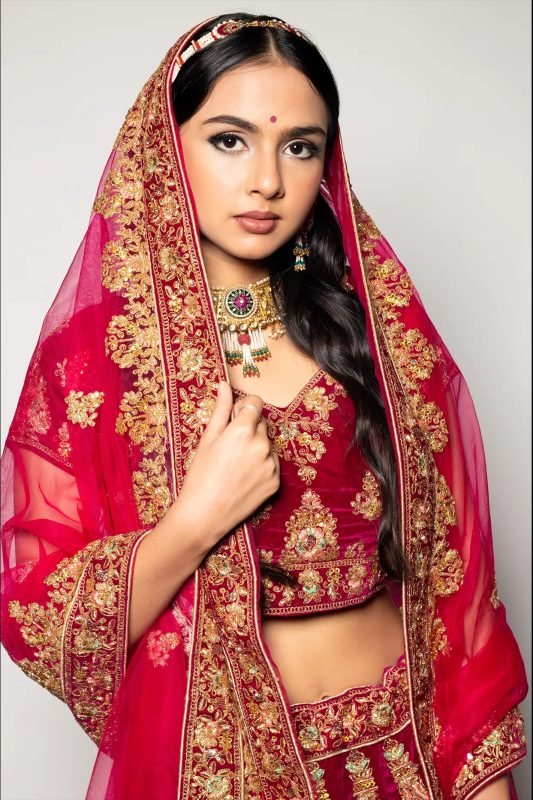 Bridal makeup: a model in red and gold, dupatta over the head, hand resting at the chest