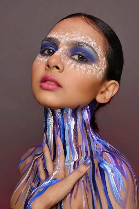 Editorial makeup: blue and purple paint running down the neck, one hand at the chest