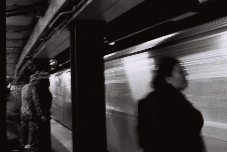 Black and white: a subway platform with a train rushing past, commuters blurred by the motion