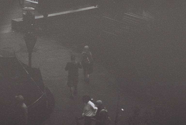 Black and white: figures walking through a fog-filled street at night