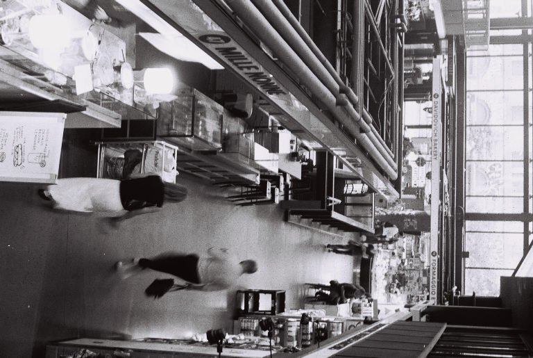 Black and white: the tilted interior of a diner, staff and customers along the counter