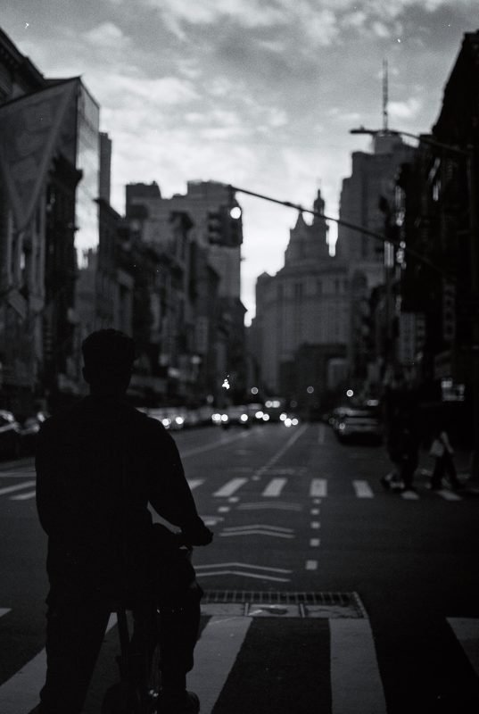 Black and white: the silhouette of a person waiting at a crossing on a wide city street