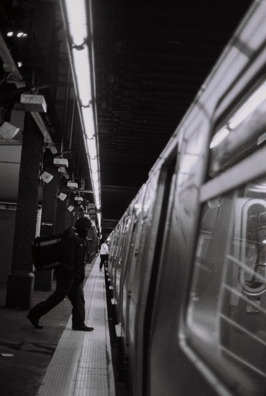 Black and white: a subway platform, a lone figure walking beside a waiting train