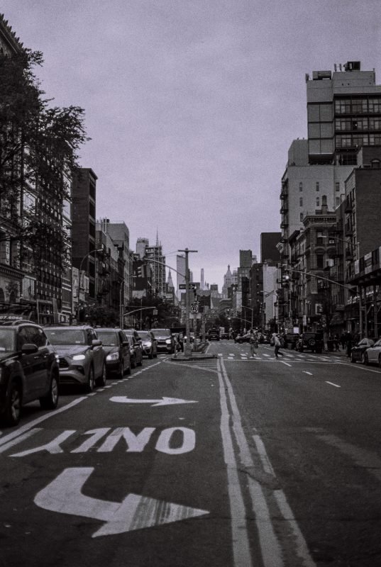 A city street marked ONLY with a turn arrow, parked cars either side and towers ahead