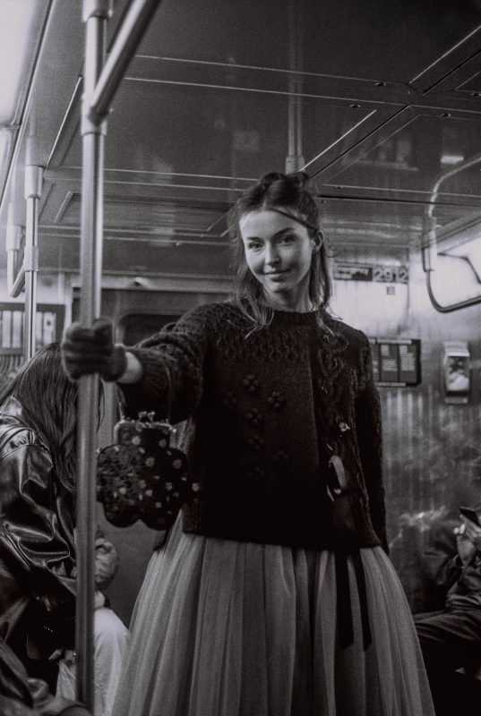 Black and white: a woman holding the pole aboard a tram, smiling toward the camera