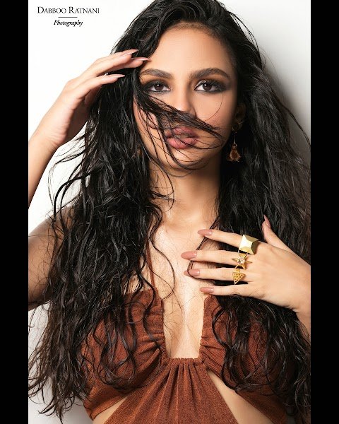 Close portrait of Sargam in a brown textured dress, hair swept across her face, gold rings on her hand