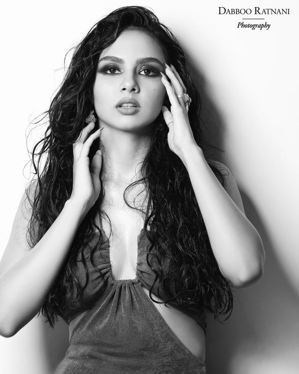 Black and white portrait of Sargam with her hands lifted into her hair against a dark backdrop