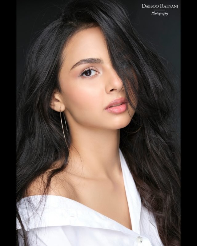 Sargam in a white shirt worn off one shoulder, hair loose against a dark backdrop