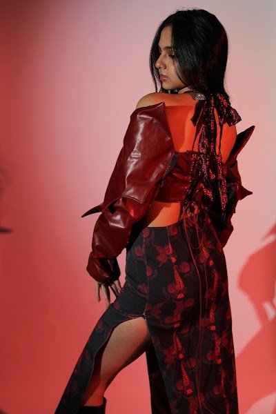 Rea by Rhea lookbook: a model turning away in a red leather jacket and floral slit skirt