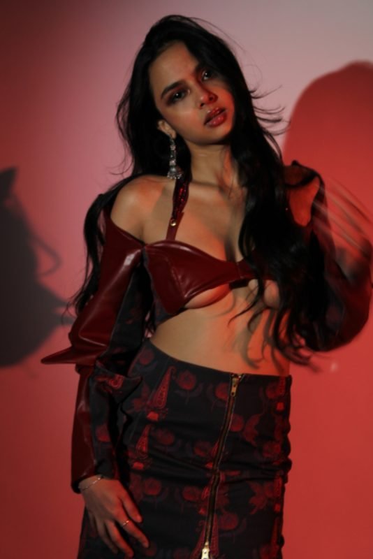 Rea by Rhea lookbook: a red leather bandeau and cropped jacket with a dark floral skirt, red backdrop