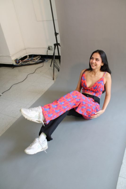 Rea by Rhea lookbook: a model seated on the studio floor in a red printed co-ord and white trainers
