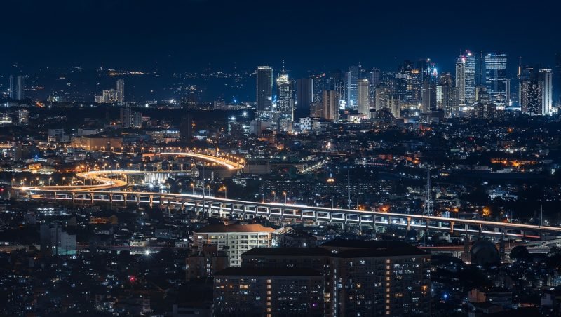 A city skyline at night, lit towers above a lit highway